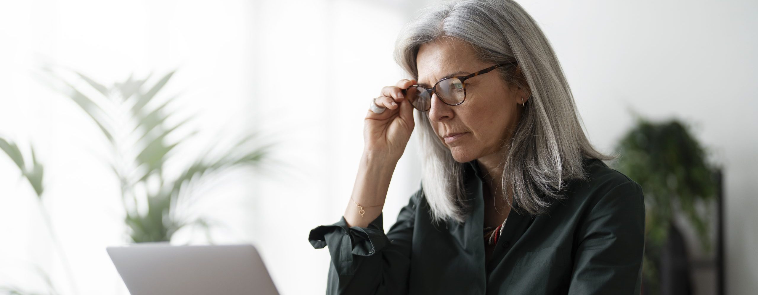 A person looking at a screen with one hand about to take off or in the proces of putting on glasses. Concenrating.