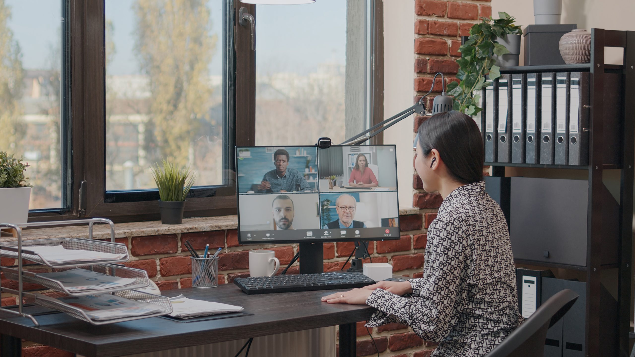 A person taking part in an online meeting. There are four people on a screen in front of the person and they have ear buds in.